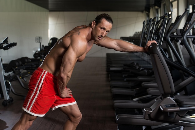 Muscular Mature Man Doing Heavy Weight Exercise For Back With Dumbbell In Modern Fitness Center