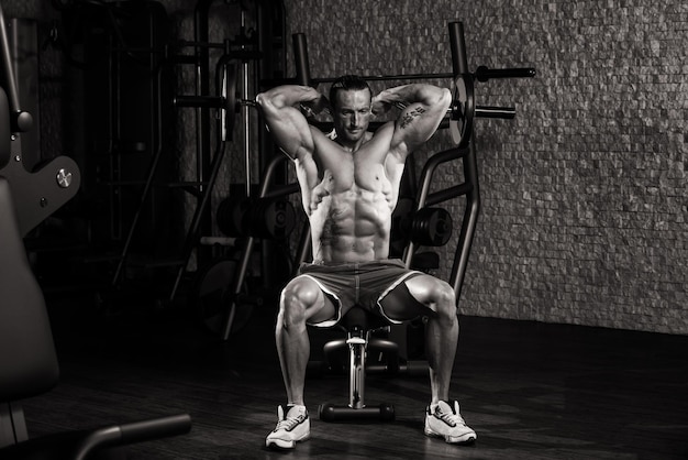 Мускулистый взрослый мужчина делает тяжелые упражнения для трицепсов в современном фитнес-центре