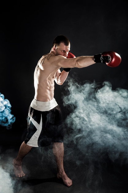 Muscular muay thai fighter punching in smoke