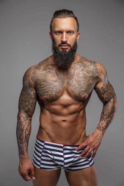 Muscular nude man with tattooed body isolated on grey background.