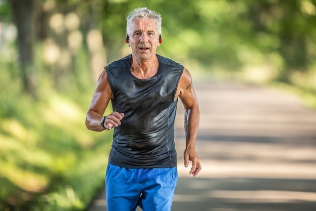 Muscular older man in good shape runs outdoors and sweats during a run with his earphones on.