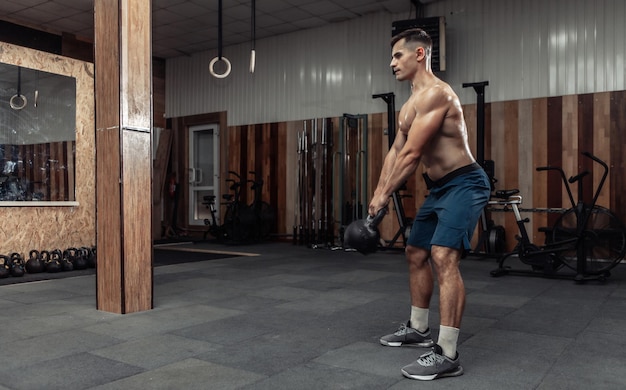 Muscular powerful man exercising with heavy kettlebell in cross fit gym. Functional training with free weights