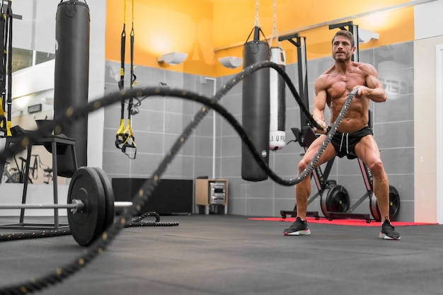 Muscular powerful man working out with rope in functional training fitness gym