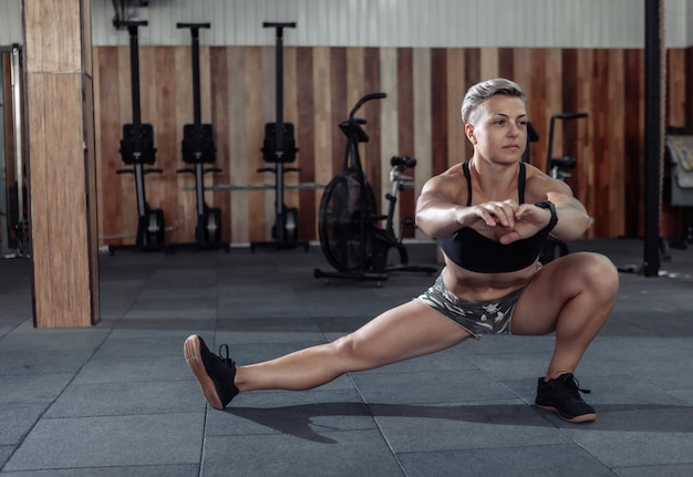 Muscular powerful woman practicing warm-up before intense workout in a modern cross-gym.