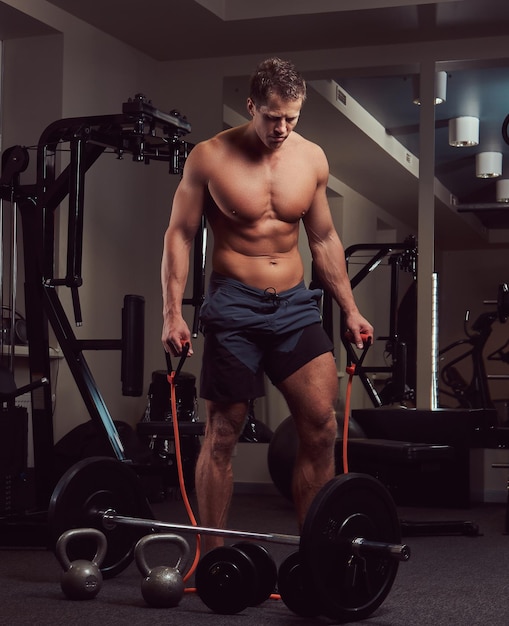 A muscular shirtless athlete doing exercise with an expander in the gym.