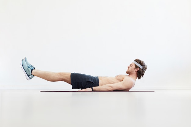 Muscular shirtless man lying on back and training his abs isolated on white background