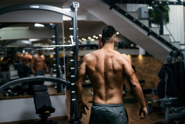 Uomo senza camicia muscolare che posa in palestra