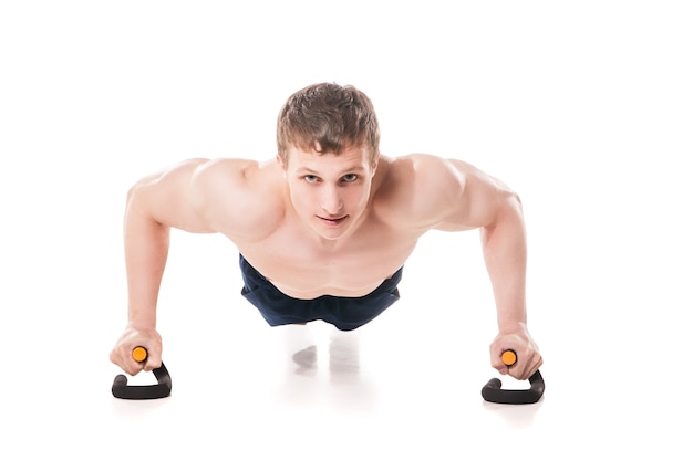 Muscular shirtless sportsman making push-ups in studio isolated on white background