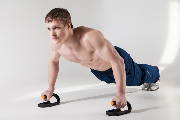 Muscular shirtless sportsman making push-ups in studio isolated on white background