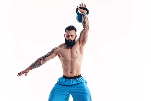 Muscular shirtless tattooed bearded male athlete bodybuilder workout with kettlebell 