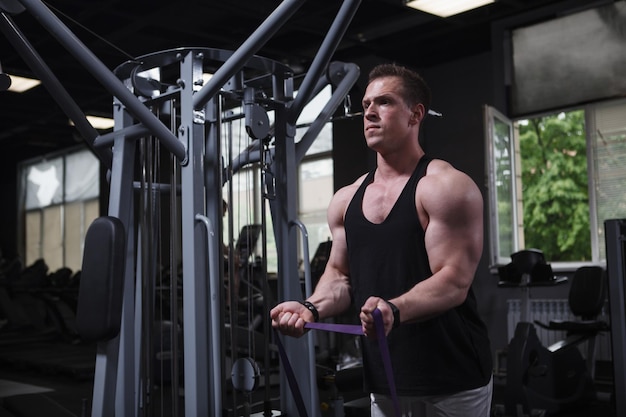 Muscular sportsman warming up at the gym doing biceps curls with resistance band