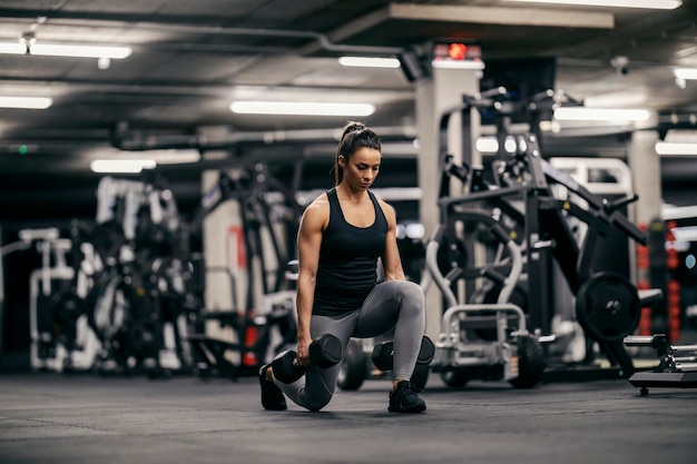 A muscular sportswoman is lifting dumbbells and doing lunges in a gym