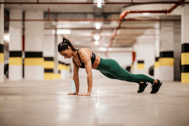 A muscular sportswoman in shape is doing pushups in underground garage
