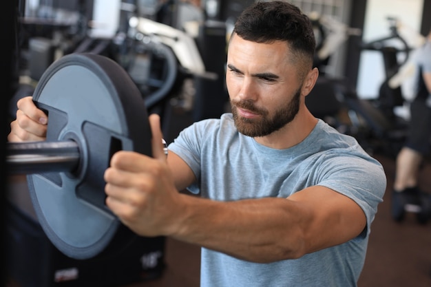 Muscular sporty indian man adding weight on barbell at gym.