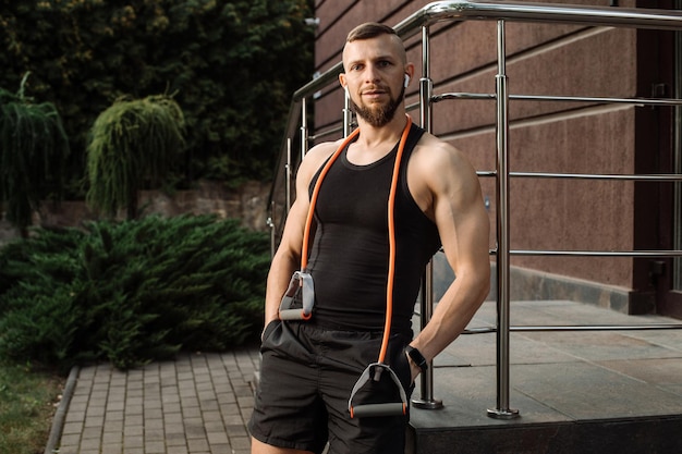 Muscular sporty male is posing with a stretching rubber outdoors after trainings