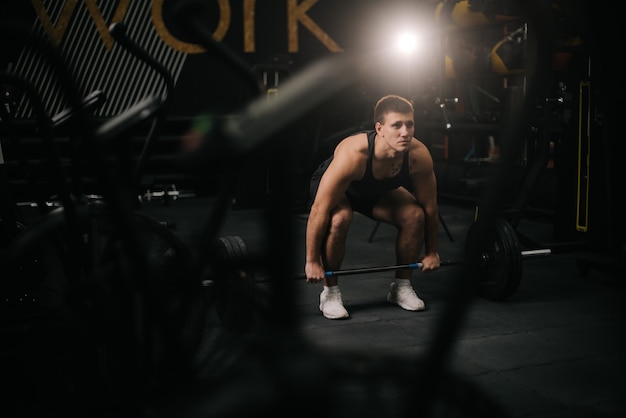 Muscular strong man with perfect beautiful body wearing sportswear lifting heavy barbell from floor