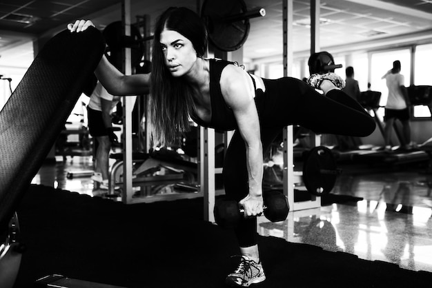 Photo muscular woman exercising back and legs with dumbbells