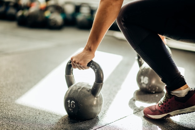 Muscular woman holding old and rusty kettle bell on to the gym floor