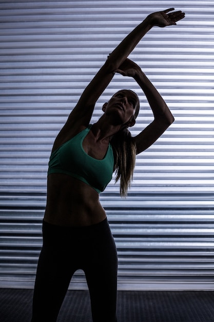 Muscular woman stretching in shadow room 