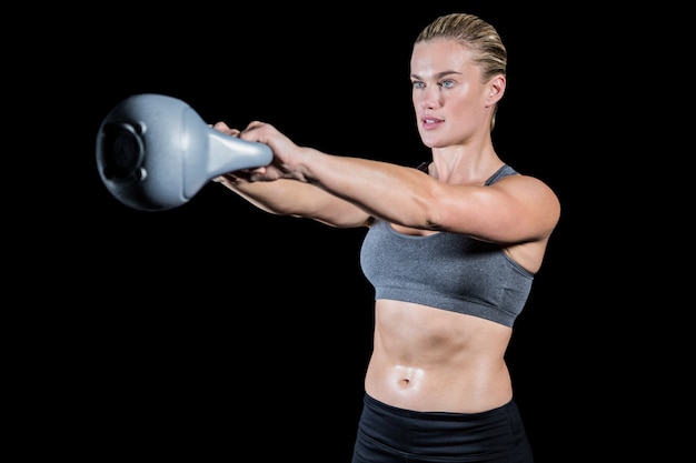 Muscular woman swinging heavy kettlebell on black background