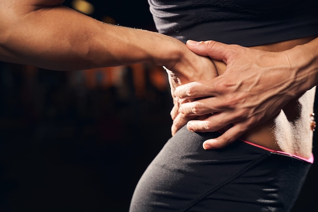 a muscular woman wearing sport clothes holding on to her back at the gym