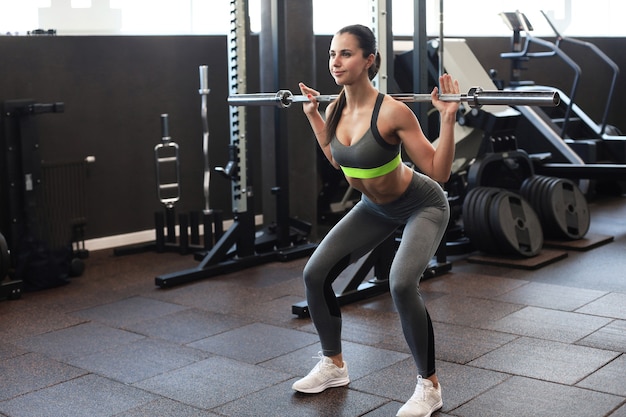 Muscular woman working out in gym doing exercises with barbell at biceps.