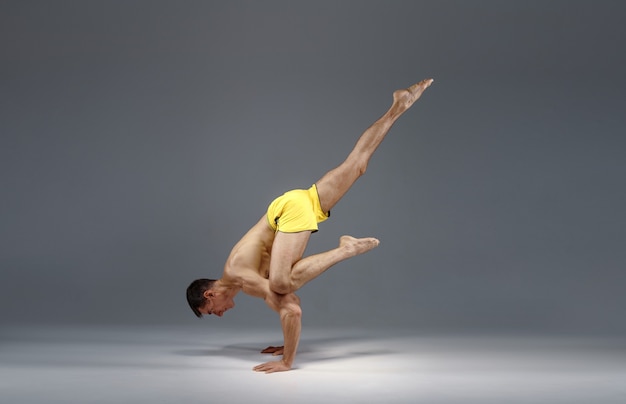 Muscular yoga stands on hands in difficult pose, meditation position, grey background.