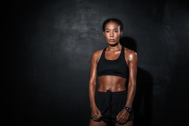 muscular young african sportswoman standing isolated on black