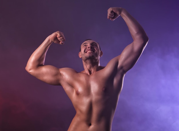 Muscular young bodybuilder in colorful smoke