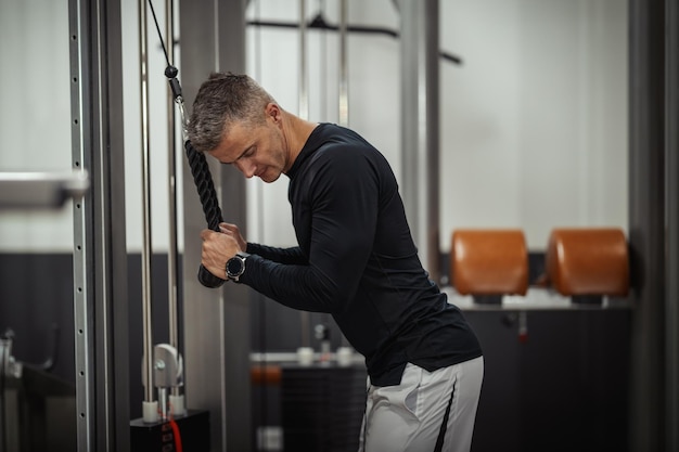 Muscular young man doing exercises for triceps on cable machine during a strength training workout at the gym.