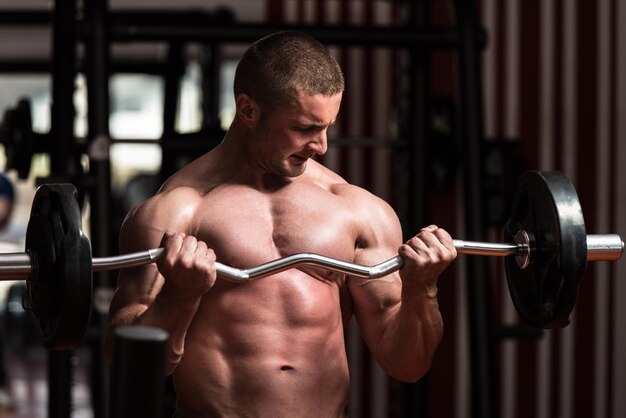 Muscular Young Man Doing Heavy Weight Exercise For Biceps In Gym