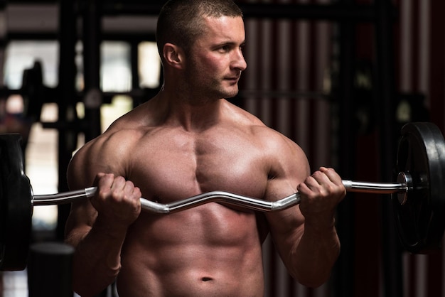 Muscular Young Man Doing Heavy Weight Exercise For Biceps In Gym