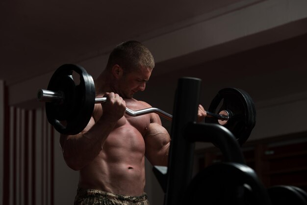 Muscular Young Man Doing Heavy Weight Exercise For Biceps In Gym