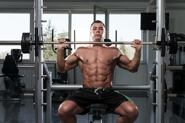 Muscular Young Man Doing Heavy Weight Exercise For Shoulders In Gym