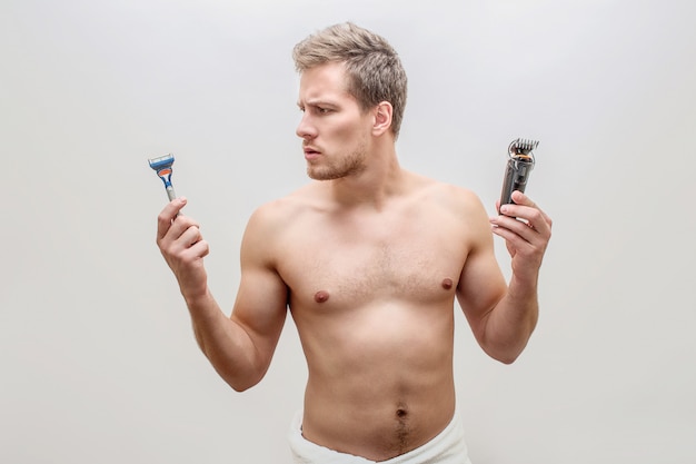 Photo muscular young man hold razers and shving machine in both hands