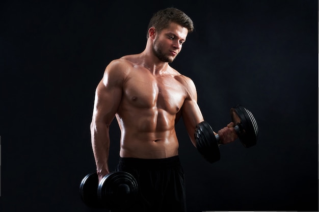 Muscular young man lifting weights on black background