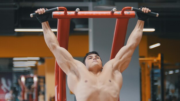 Muscular young man pulling up in a gym close up