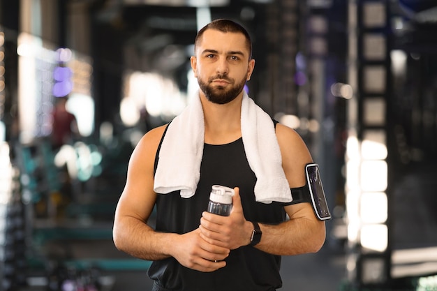 Foto giovane muscoloso in piedi in palestra con una bottiglia d'acqua in mano