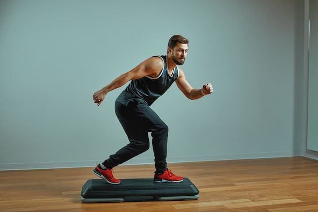 Muscular young man training on step platforms on the gray background in the studio