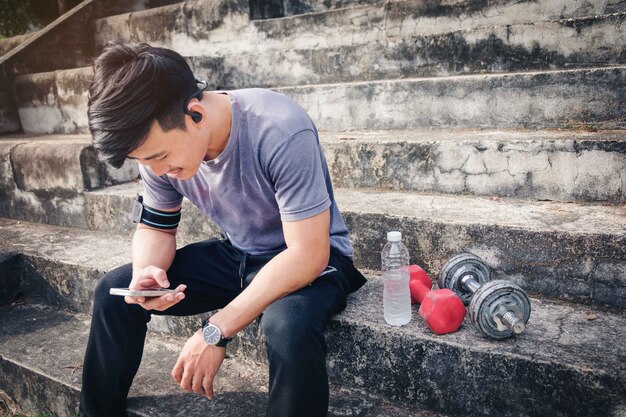  Muscular young man using smartphone in the park before training