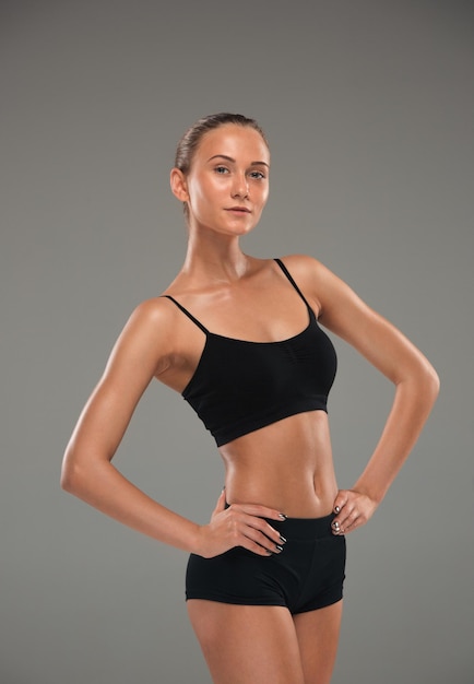 Muscular young woman athlete posing on gray studio background