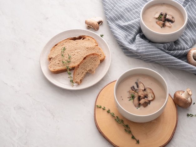 Mushroom cream soup in white bowl with bread on the table. 