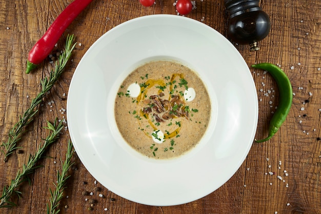 Mushroom cream soup with champignons, garnished with fried mushrooms, olive oil and grated Parmesan cheese in grey bowl on a wooden surface