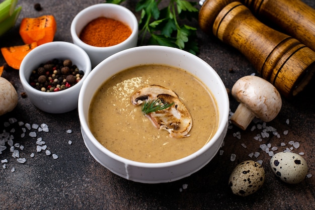 Foto purea di zuppa di funghi in un piatto con ingredienti sui lati su un tavolo nero.