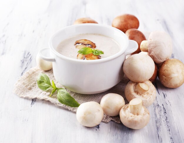 Mushroom soup in white pot on napkin on wooden background