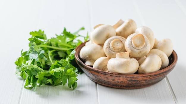 Mushrooms in a bowl with parsley leaves on a white wooden table