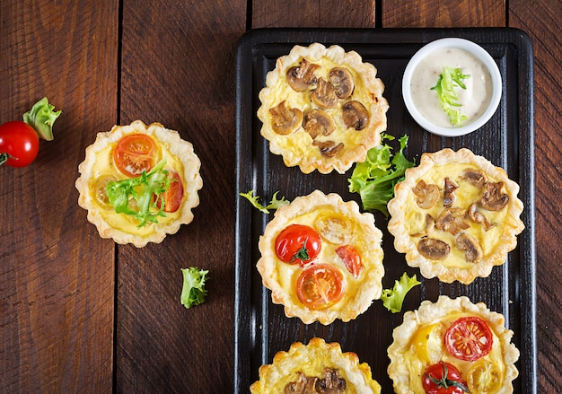 Mushrooms, cheddar, tomatoes tartlets on wooden table.