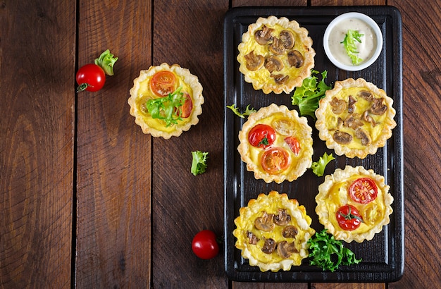 Mushrooms, cheddar, tomatoes tartlets on wooden