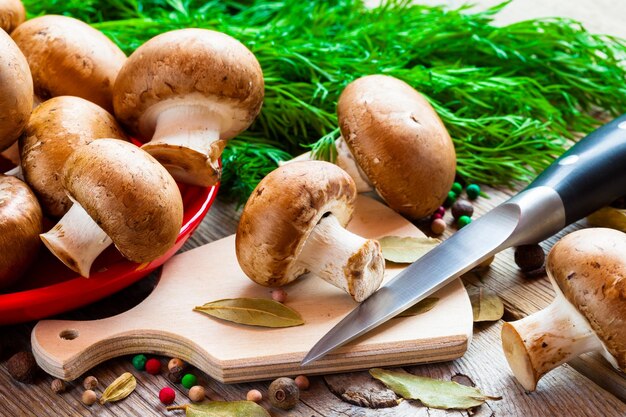 Mushrooms on cutting board knife dill and spices on wooden table