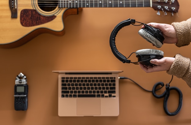 Music background with headphones in female hands, recorder, laptop and guitar, flat lay.
